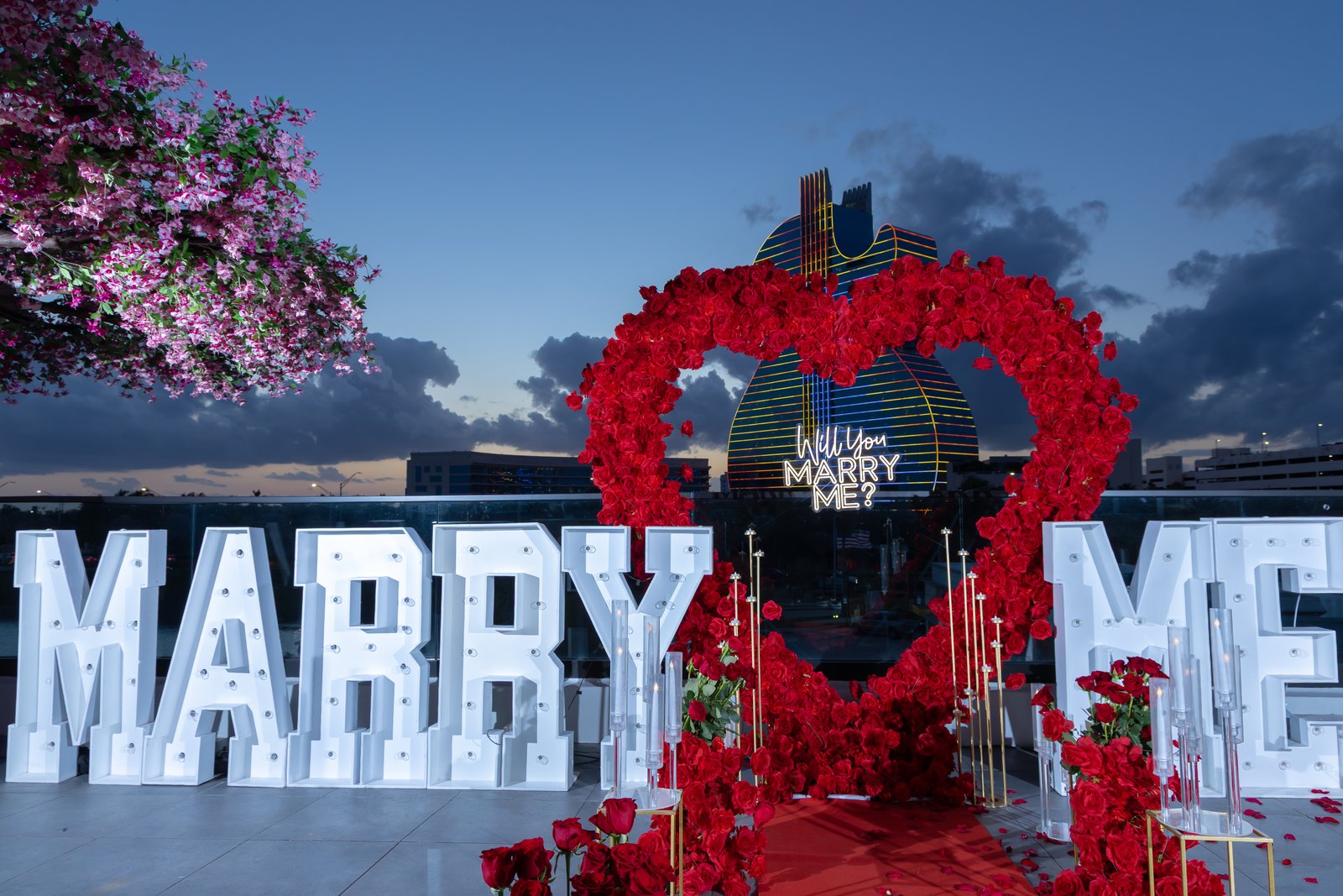 Proposal setup with rose heart arch and Will You Marry Me sign at sunset